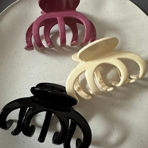 Three glossy pumpkin-shaped hair claw clips in rose, cream and black on a tray