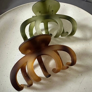 Close-up of large 10cm matte hair claws in olive green and dark brown on a ceramic tray