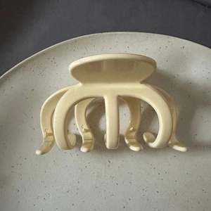 Detail of a large matte cream hair claw clip placed on a decorative ceramic plate