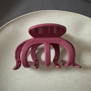 Top view of shiny rose pink claw clip with multi-claw design on a textured background