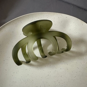 Macro view of olive green matte shark hair clip on a minimalist ceramic tray