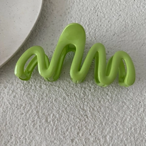 Dettaglio di un fermaglio a onde verde erba da 13 cm su una superficie bianca