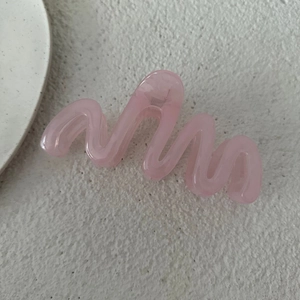 Dettaglio della molletta per capelli rosa ondulata in resina su trama di pietra naturale