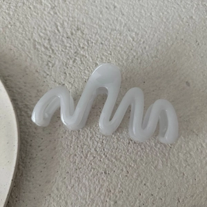 Dettaglio ravvicinato di una pinza per capelli bianca da 13cm con design a onda opaca