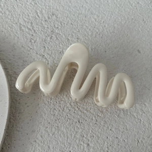 Dettaglio macro di un fermaglio per capelli ondulato da 13 cm crema su pietra ruvida
