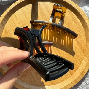 Grandi pinze per capelli nero opaco e tartarugate esposte su un vassoio di legno naturale
