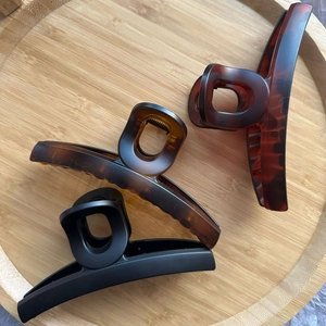 Trois grandes pinces à cheveux mates en écaille et noir sur un plateau en bois