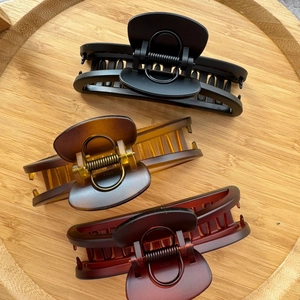 Three large matte crescent hair claws in black, amber, and red on a round wooden tray