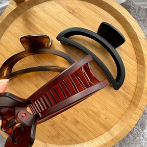 Close-up of large matte black and tortoiseshell claw clips on a wooden tray for thick hair