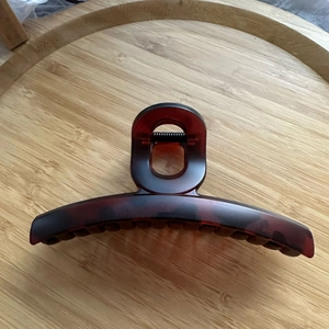 Détail d'une grande pince à cheveux mate rouge foncé sur un plateau en bois épuré