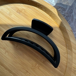 Close-up of a matte black crescent shark clip on a wooden tray with elegant natural shadows