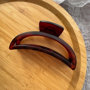Detail of a large amber crescent hair claw clip on a wooden tray with neutral tones