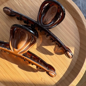Elegant amber tortoiseshell hair claws in glossy resin on a spiral wooden tray