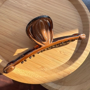 Detail of a large amber tortoiseshell hair claw clip on a bamboo tray with glossy finish