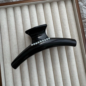 Elegant black glossy hair claw clip with pearls on beige velvet jewelry display tray