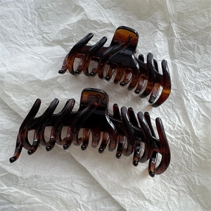 Close-up of two large tortoise shell hair claws with strong teeth on white paper