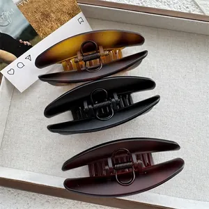 Three oversized hair claws in tortoiseshell and matte black on a beige wooden tray