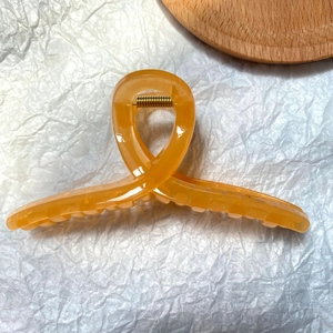 Detail of translucent orange hair claw clip with golden metal spring on white background