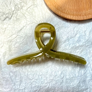 Detail of an olive green jelly-colored hair claw clip with golden metal spring