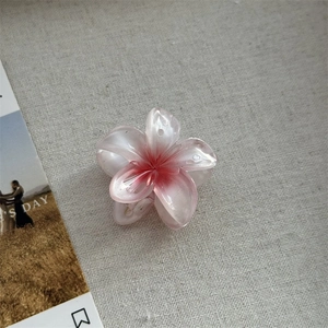Détail macro d'une pince à cheveux en forme de fleur de frangipanier avec dégradé nacré rose