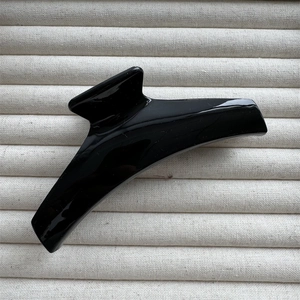 Gros plan d'une pince à cheveux noire brillante au design minimaliste sur un fond beige texturé