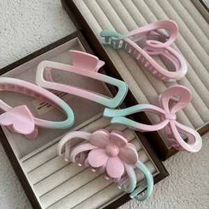 Close-up of five gradient pink and green hair claws in various shapes within a display box