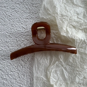 Close-up of a glossy amber hair claw clip with a strong golden metal spring detail