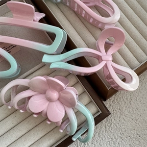 Macro shot of pink and green gradient hair claws with floral and bow designs on beige tray