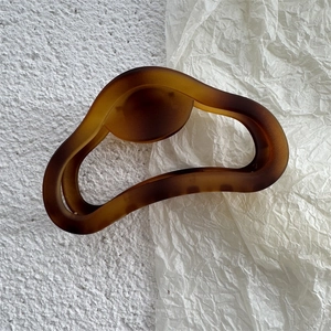 Macro di una grande clip per capelli ambra opaca con trama a onde irregolari su carta