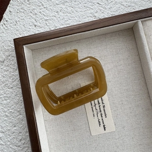 Gros plan d'une pince à cheveux rectangulaire en acétate ambré sur un plateau blanc