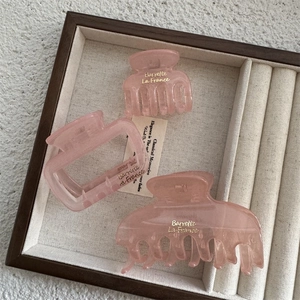 Three-piece set of translucent pink hair claws with gold lettering on a display tray