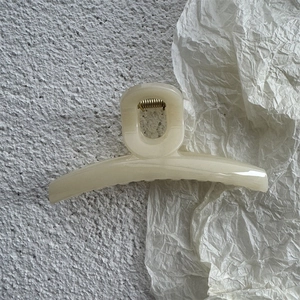 Close-up of cream white marbled hair claw clip with golden metal spring on textured background