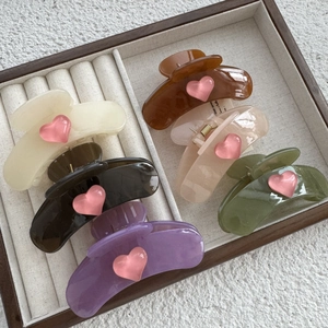 Set of six colorful heart hair claws in cream, pink, and green on a velvet tray
