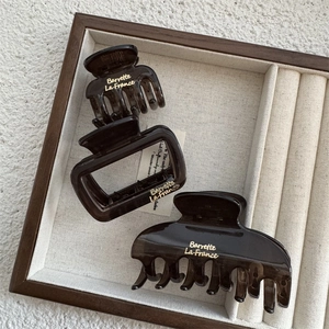 Three-piece set of brown tortoiseshell hair claws with gold lettering on wooden tray