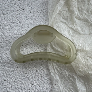 Dettaglio di una pinza per capelli verde chiaro opaca con texture satinata e molla in metallo