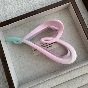 Close-up of heart-shaped gradient hair claw clip in mint green and pink on a wooden tray