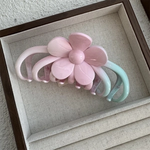 Close-up of pink and green gradient flower hair claw clip on a soft beige display tray