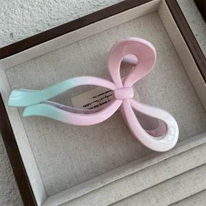 Close-up of pink and green gradient bow-shaped hair claw clip on a wooden display tray