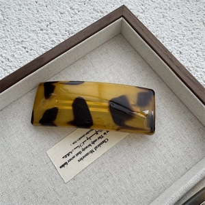Close-up of tortoise shell pattern on a square hair clip in a wooden jewelry tray