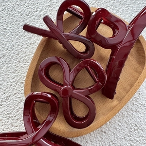 Close-up of assorted burgundy resin hair claws with glossy finish on a wooden tray
