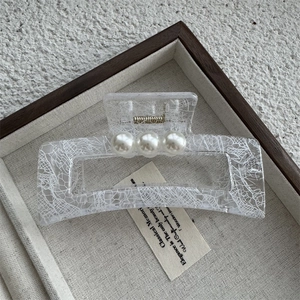 Détail d'une pince à cheveux rectangulaire transparente avec dentelle et trois perles