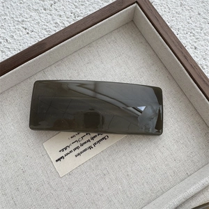 Close-up of polished dark brown translucent square hair clip on a minimalist linen tray