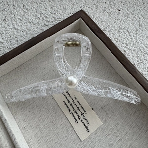 Détail d'une pince à cheveux transparente avec motif dentelle et perle centrale élégante