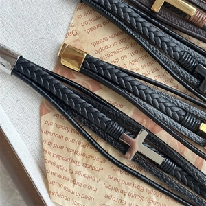 Macro detail of multi-layer braided leather bracelets with silver cross and metal clasps