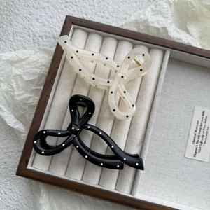 Close-up of retro polka dot bow hair claws in black and cream on a wooden jewelry tray