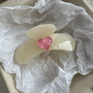 Detail shot of a cream jelly claw clip with a pink heart on a white textured background