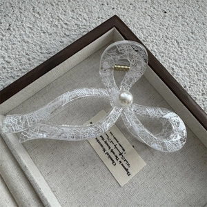 Détail d'une pince à cheveux transparente avec motif dentelle blanche et perle centrale
