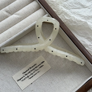 Detail of cream white polka dot hair claw clip showing acetate texture and metal spring