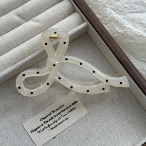 Detailed close-up of cream white polka dot hair claw clip on a linen jewelry tray