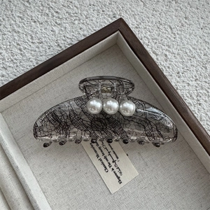 Détail de la pince à cheveux grise à motif dentelle avec trois perles blanches sur texture